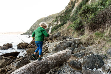 Curly haired child walking on log near ocean in New Zealand - CAVF83301