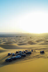 Menschen beobachten den Sonnenuntergang in der marokkanischen Wüste von ihren 4x4-Fahrzeugen aus - CAVF83352