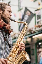 Vertikales Foto eines Saxophonisten mit Bart und blondem Haar, der auf der Straße spielt - CAVF83364