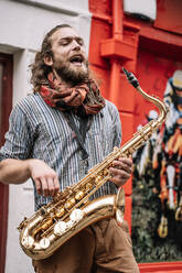 Vertikales Foto eines Saxophonisten, der mit emotionalem Ausdruck auf der Straße singt - CAVF83367
