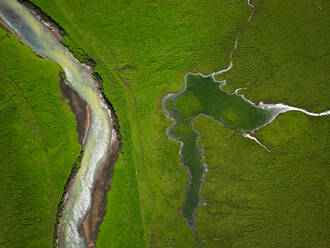 Aerial shot from river running through green field - CAVF83412
