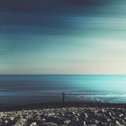 Germany, Lower Saxony, Neuharlingersiel, Silhouette of man standing alone on rocky coastal beach - DWIF01099