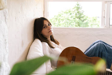 Porträt einer Frau mit Gitarre, die auf einem Bett sitzt und sich entspannt - ERRF03922