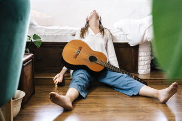 Woman with guitar sitting on the floor in front of bed - ERRF03928