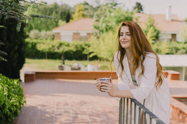 Portrait of redheaded woman with cup leaning on railing - AFVF06387