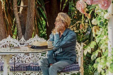 Portrait of senior woman with eyes closed relaxing on garden bench - ERRF03937