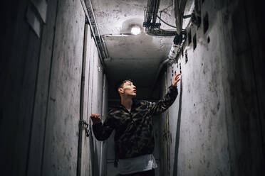Young man looking away while standing in corridor amidst old walls - MEUF00611