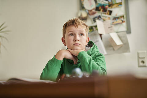 Nachdenklicher Junge, der beim Lernen zu Hause wegschaut, lizenzfreies Stockfoto