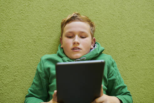 Junge benutzt digitales Tablet auf grünem Teppich zu Hause - MMIF00272