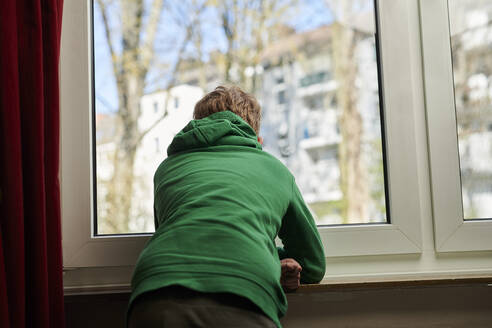 Boy looking out through window at home - MMIF00275