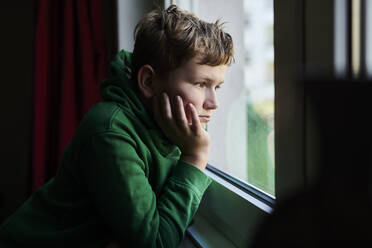 Gelangweilter Junge schaut zu Hause aus dem Fenster - MMIF00277