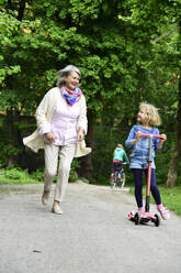 Active senior woman running while granddaughter riding push scooter in park - ECPF00945