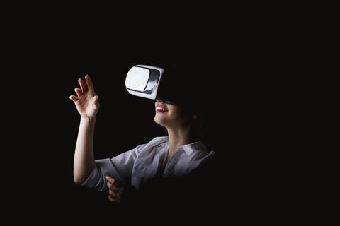 Junge Frau mit VR-Brille vor schwarzem Hintergrund, lizenzfreies Stockfoto