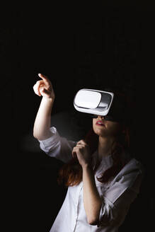 Junge Frau gestikuliert, während sie eine VR-Brille auf schwarzem Hintergrund benutzt - LJF01532
