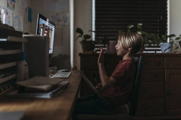 Side view of young boy waving to friends on video chat - CAVF83472