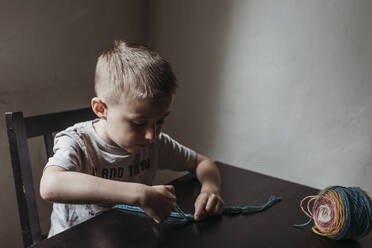 Young boy knitting with fingers at home during isolation - CAVF83483