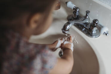 Young preschool aged girl washing hands in sink with soap - CAVF83488