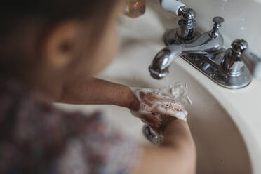 High angle of preschool aged girl washing hands in sink with soap - CAVF83490