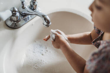 High angle view of young girl washing hands in sink with soap - CAVF83492