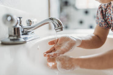 Close up view of young child washing hands with soap in sink - CAVF83495