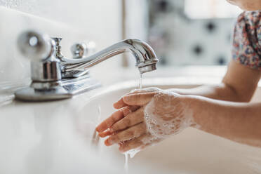Close up view of young child washing hands with soap in sink - CAVF83496