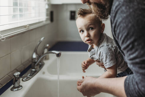 Seitenansicht eines Jungen, der sich von seinem Vater die Hände im Waschbecken waschen lässt - CAVF83499