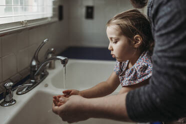 Seitenansicht eines jungen Mädchens, das sich von seinem Vater die Hände waschen lässt - CAVF83501