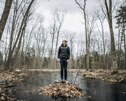 Großer Mann steht auf einem Baumstumpf inmitten eines Sumpfes an einem kalten, bewölkten Tag - CAVF83608