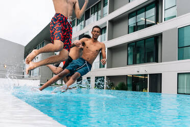 Three teenagers jumping into a pool surrounded by buildings - CAVF83620