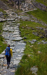 Woman with rucksack hiking up rocky path - CAVF83627