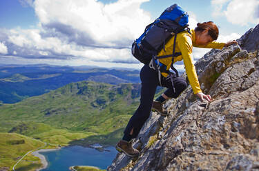 Frau mit Rucksack kraxelt auf den Berg in Snowdonia - CAVF83629