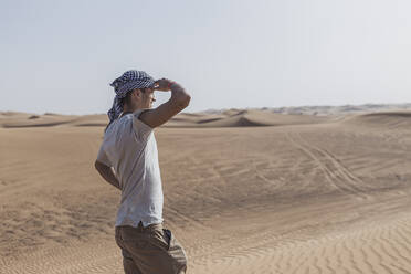 Männlicher Tourist, der seine Augen abschirmt, während er auf Sanddünen in der Wüste von Dubai, Vereinigte Arabische Emirate, steht - SNF00242