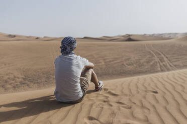 Männlicher Tourist sitzt auf Sanddünen in der Wüste von Dubai, Vereinigte Arabische Emirate - SNF00245