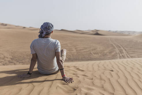 Junger Mann sitzt auf Sanddünen in der Wüste von Dubai, Vereinigte Arabische Emirate - SNF00246