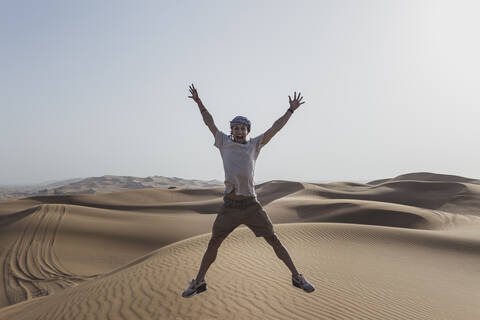 Aufgeregter männlicher Tourist springt auf Sanddünen in der Wüste von Dubai, Vereinigte Arabische Emirate, lizenzfreies Stockfoto