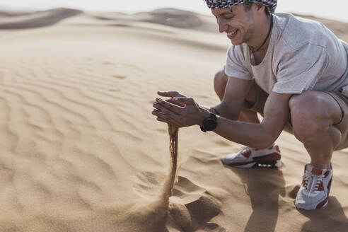 Glücklicher männlicher Tourist spielt mit Sand in der Wüste in Dubai, Vereinigte Arabische Emirate - SNF00252