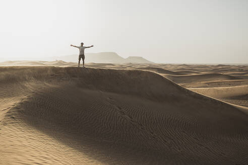 Mitteldistanz eines männlichen Touristen, der mit ausgestreckten Armen auf Sanddünen in der Wüste von Dubai, Vereinigte Arabische Emirate, steht - SNF00255