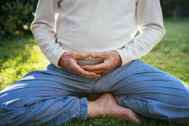 Low section of senior man meditating in garden - AFVF06392