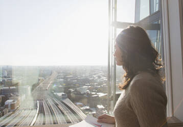 Thoughtful businesswoman at sunny window overlooking city - CAIF27529