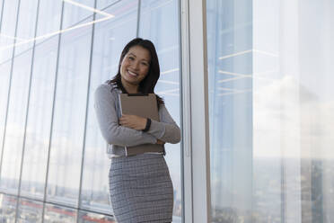 Portrait confident businesswoman with digital tablet at highrise window - CAIF27544