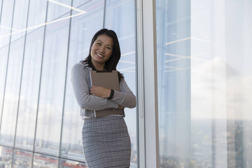 Porträt einer selbstbewussten Geschäftsfrau mit digitalem Tablet am Fenster eines Hochhauses - CAIF27544
