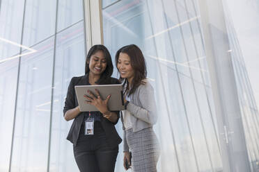 Businesswomen with digital tablet talking at office window - CAIF27558