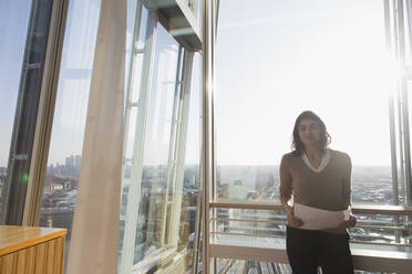 Portrait confident businesswoman at sunny highrise office window - CAIF27587