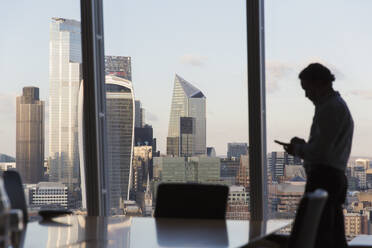 Silhouette businessman using smart phone at urban highrise window - CAIF27637