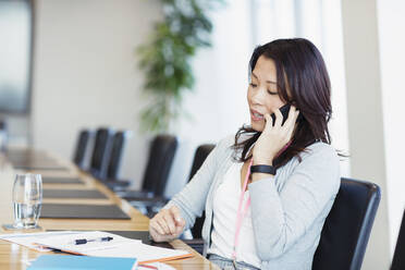 Businesswoman talking on smart phone in conference room - CAIF27638