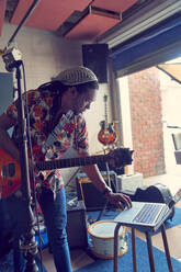 Männlicher Musiker mit Laptop und Gitarre in der Garage eines Aufnahmestudios - CAIF27676