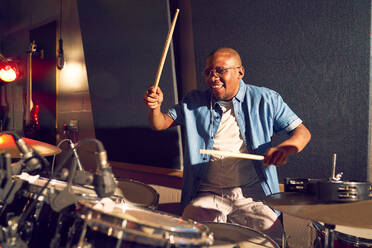 Smiling young male drummer playing drums in recording studio - CAIF27711