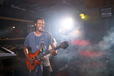 Lächelnder männlicher Musiker spielt E-Gitarre im Aufnahmestudio - CAIF27713