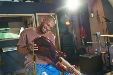 Lächelnder männlicher Musiker inspiziert Gitarre im Aufnahmestudio - CAIF27715