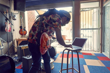 Männlicher Musiker mit Laptop und E-Gitarre im Aufnahmestudio in einer Garage - CAIF27727